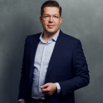 Meet the Team of experts - Photo of Jakob Rüggeberg, person in business suit, glasses, smiling, male, gallantly, standing upright